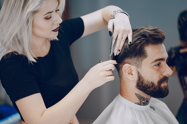 female barber triming customer's hair with a pair of scissors