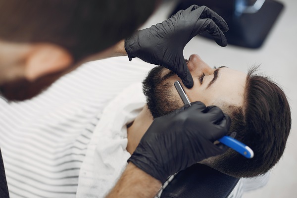 male barber triming a customer's beard using a razor